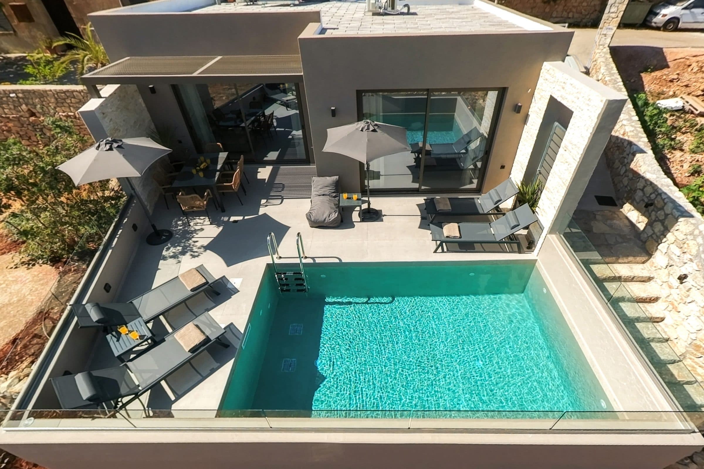 Overhead view of the terrace: two parasols, four sun loungers, the dining table and the turquoise pool
