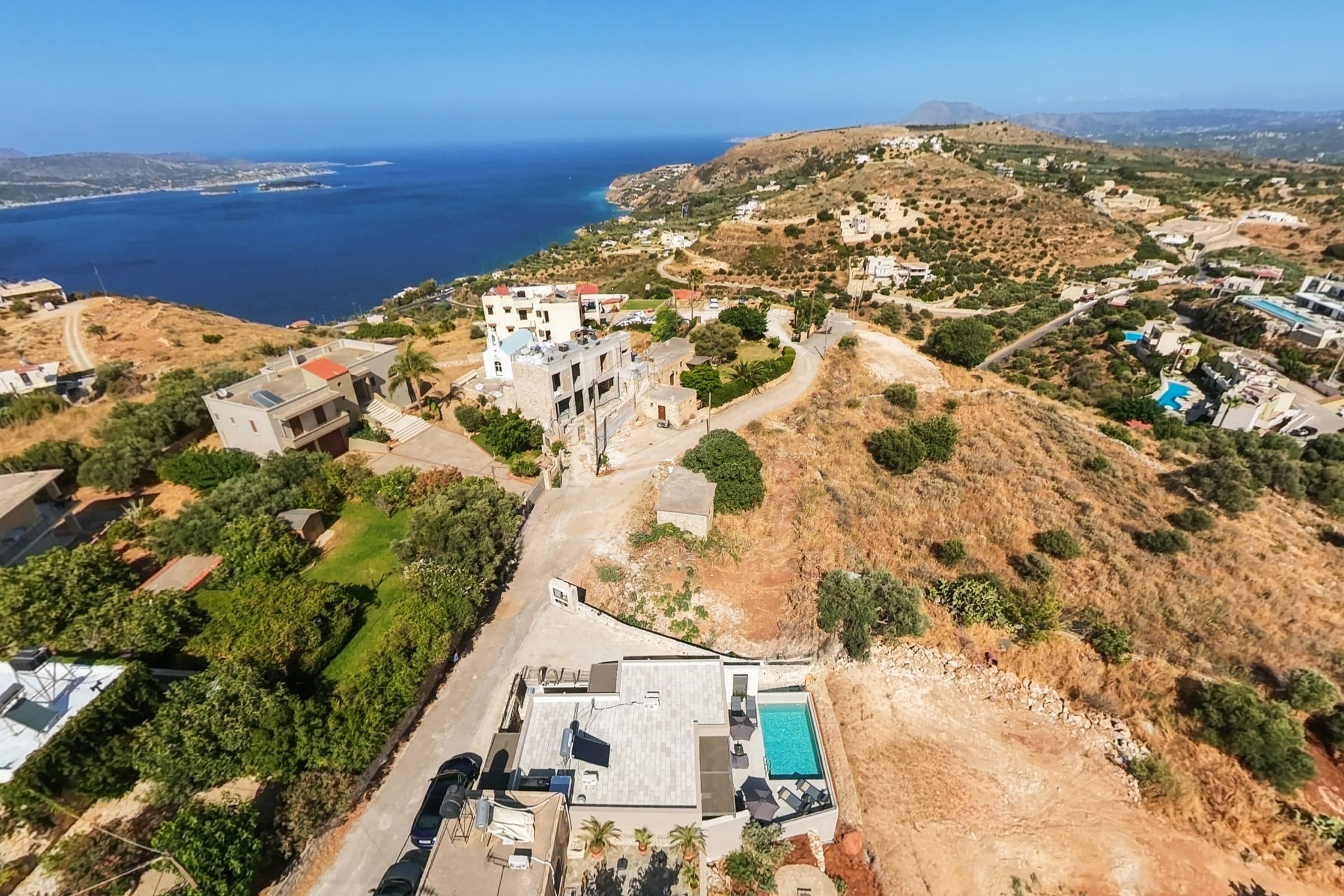 Aerial view along the coastline, with the deep blue of Souda Bay on one side and terraced olive groves on the other