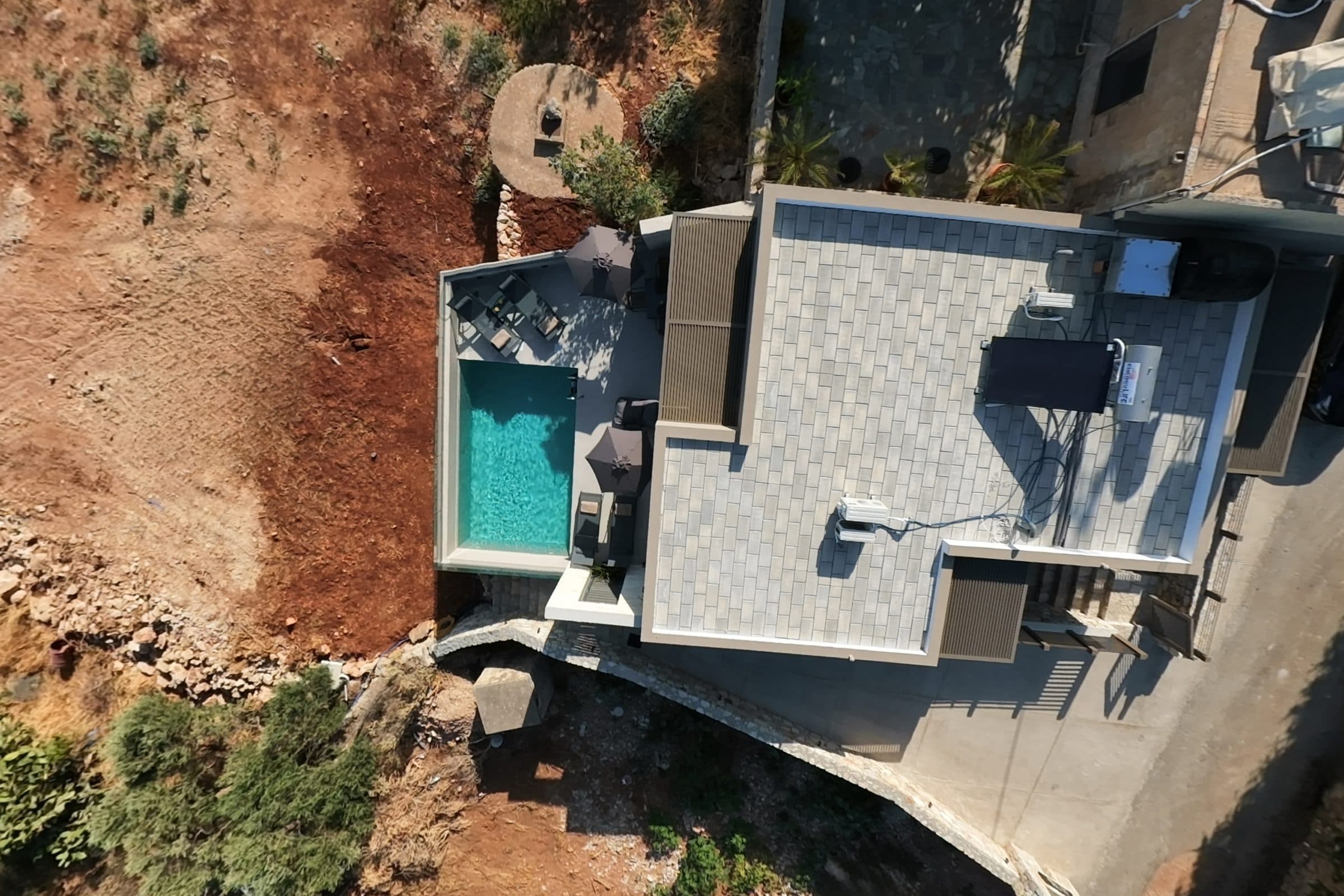 Drone view directly above the villa, showing the paved roof terrace, the pool and the dry hillside alongside