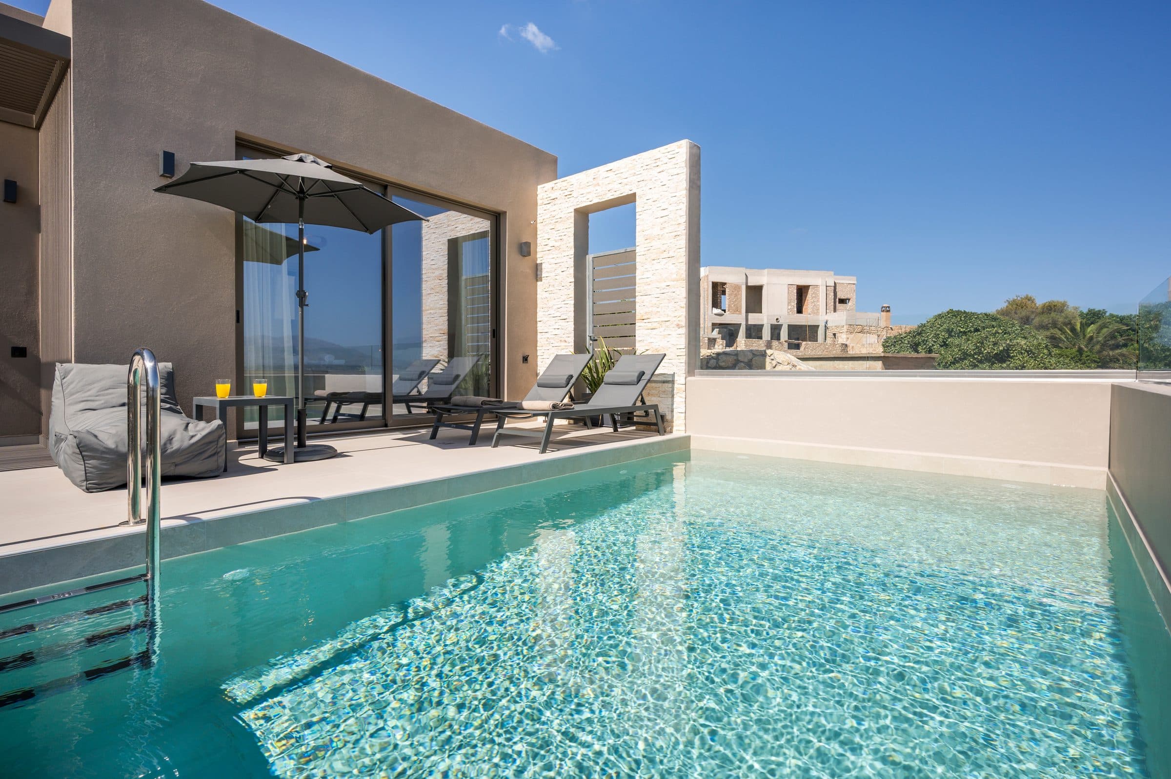 Clear turquoise water in the private pool, with the stone-clad garden wall and the sliding doors of the villa behind