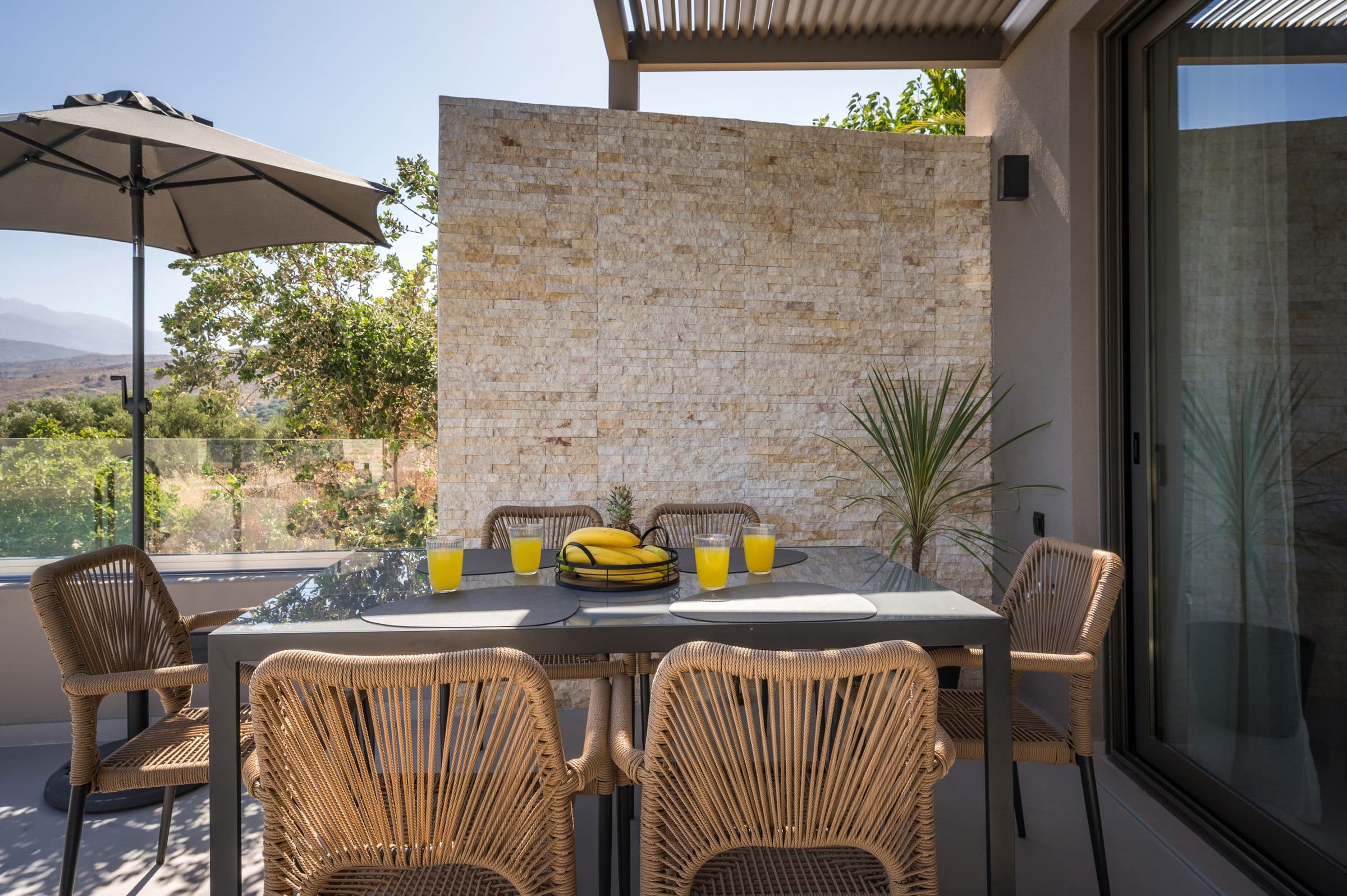 The covered terrace dining table with woven rope chairs, a bowl of fruit and a split-face stone feature wall