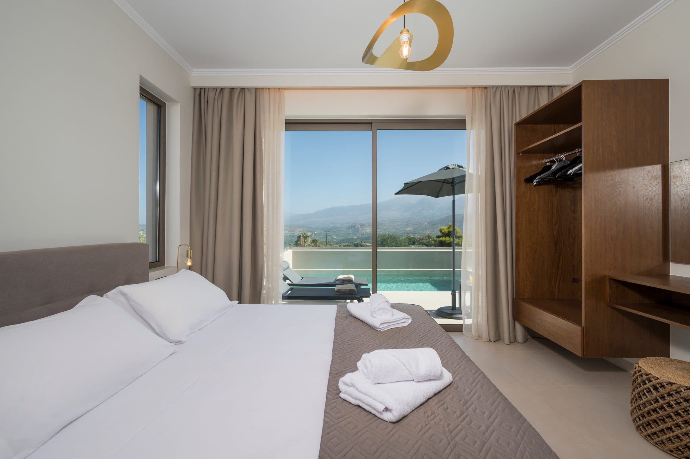 The first bedroom with a queen bed, fresh towels and sliding doors opening straight onto the pool terrace and the mountain view