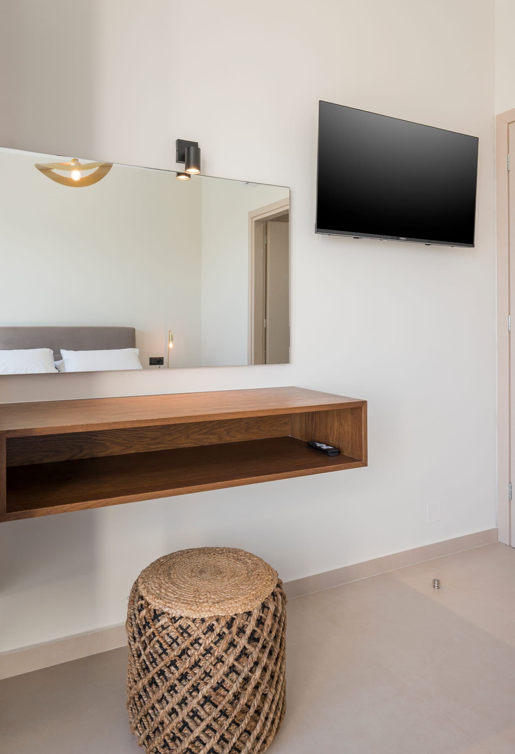 A wall mirror above a floating oak console, a flat-screen television and a woven jute stool