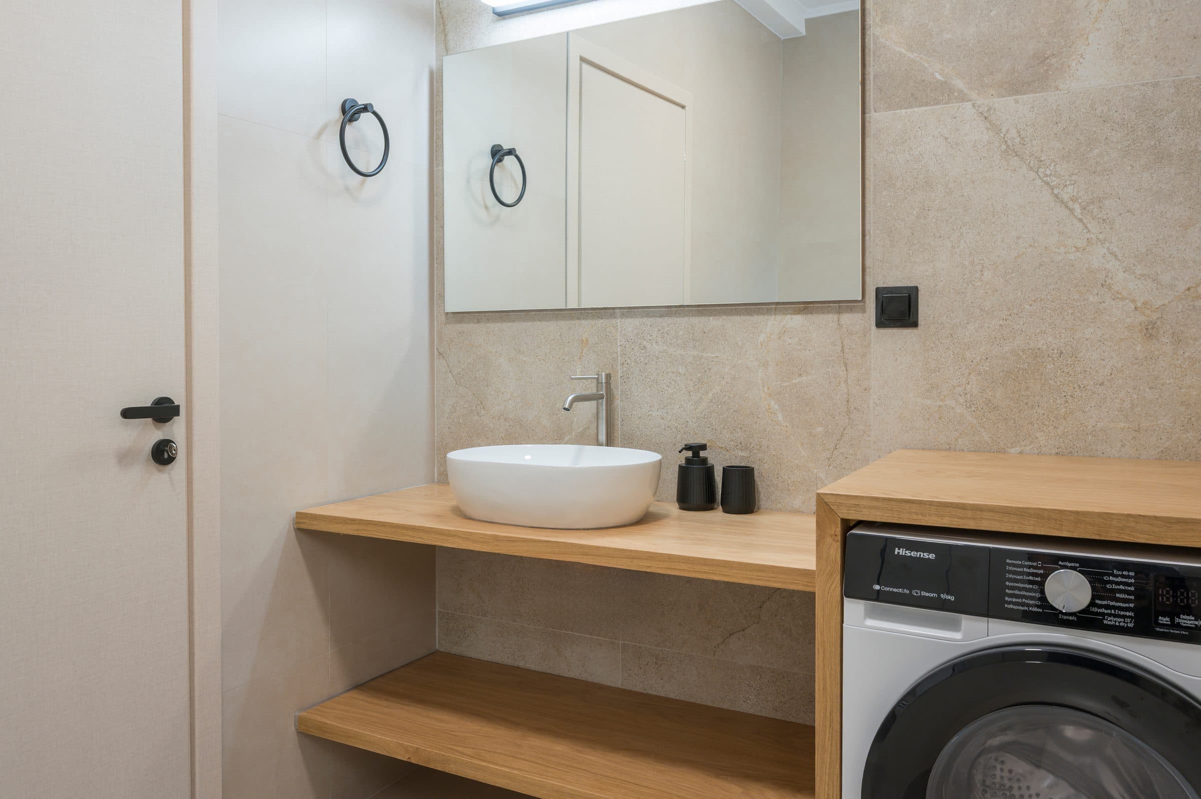 A bathroom with a round white basin on an oak shelf, a wide mirror and the washing machine built in alongside