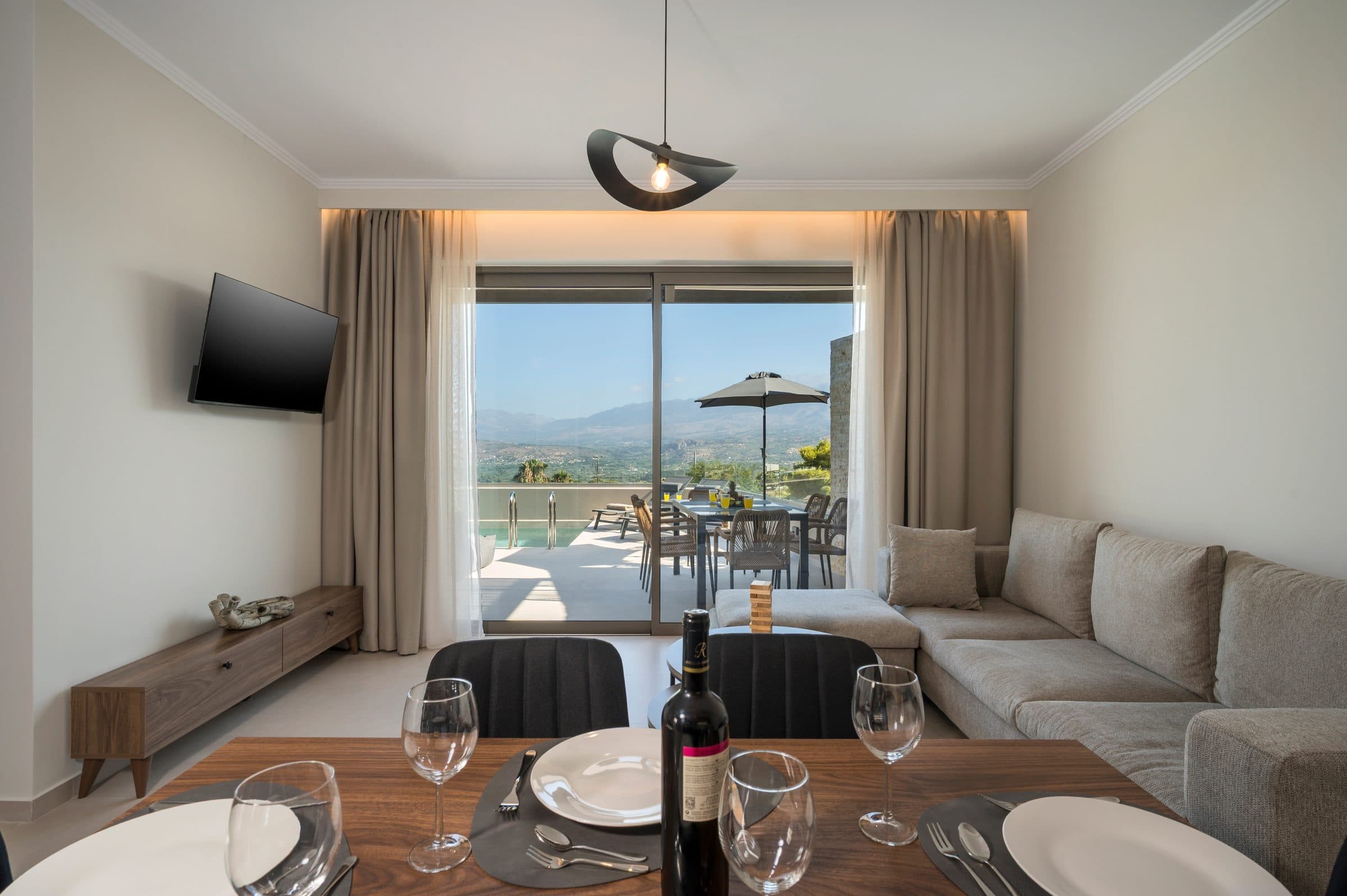 The living room with its corner sofa and laid dining table, looking through the sliding doors to the pool and the mountains