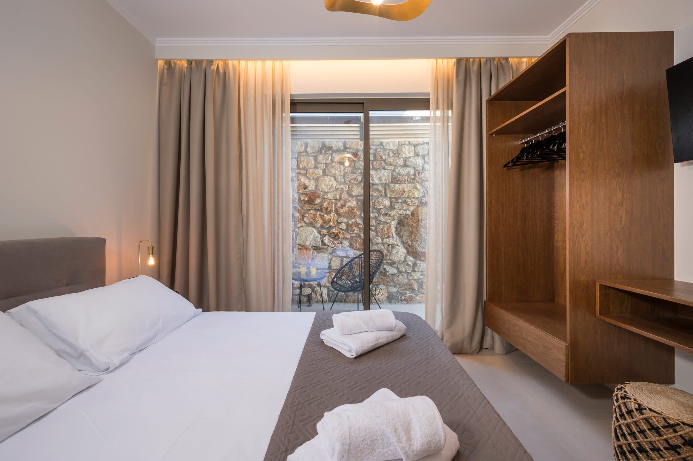 Evening in a bedroom, warm cove lighting above the curtains and the courtyard seating visible through the glass