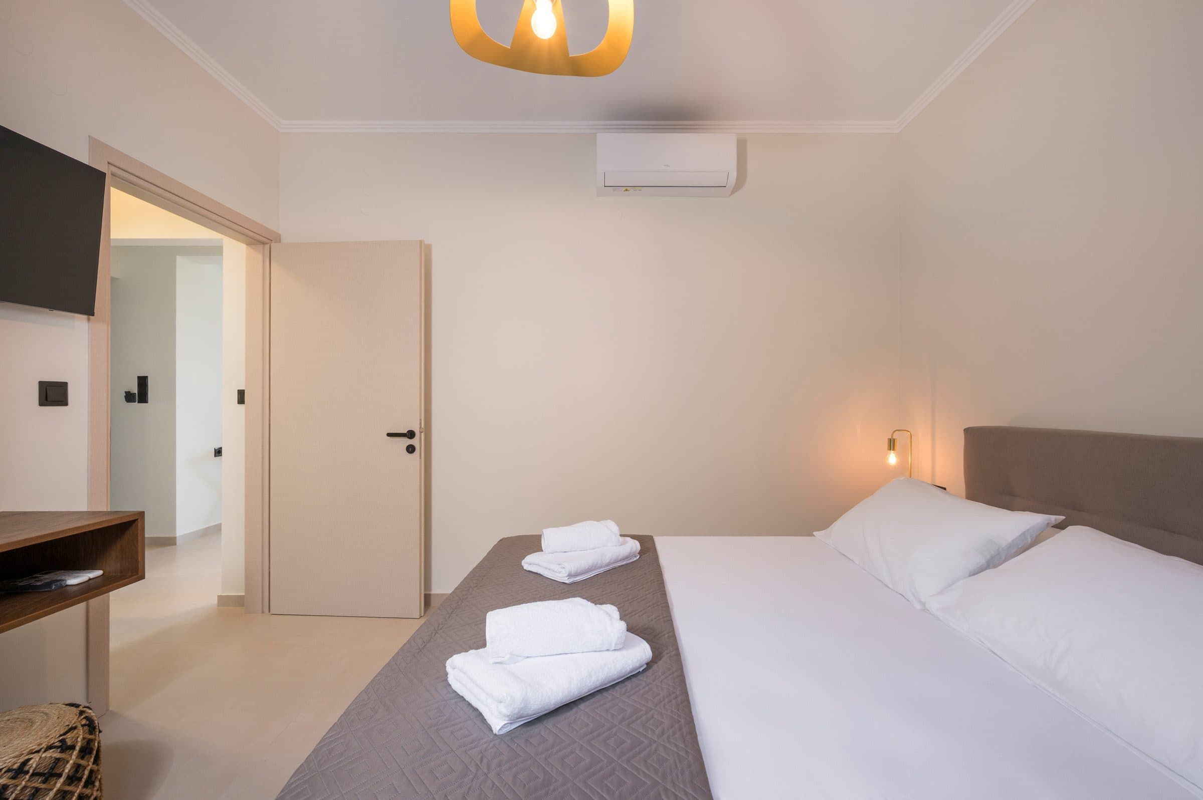 A bedroom looking towards the open door to the hallway, with the wall-mounted television and floating oak desk