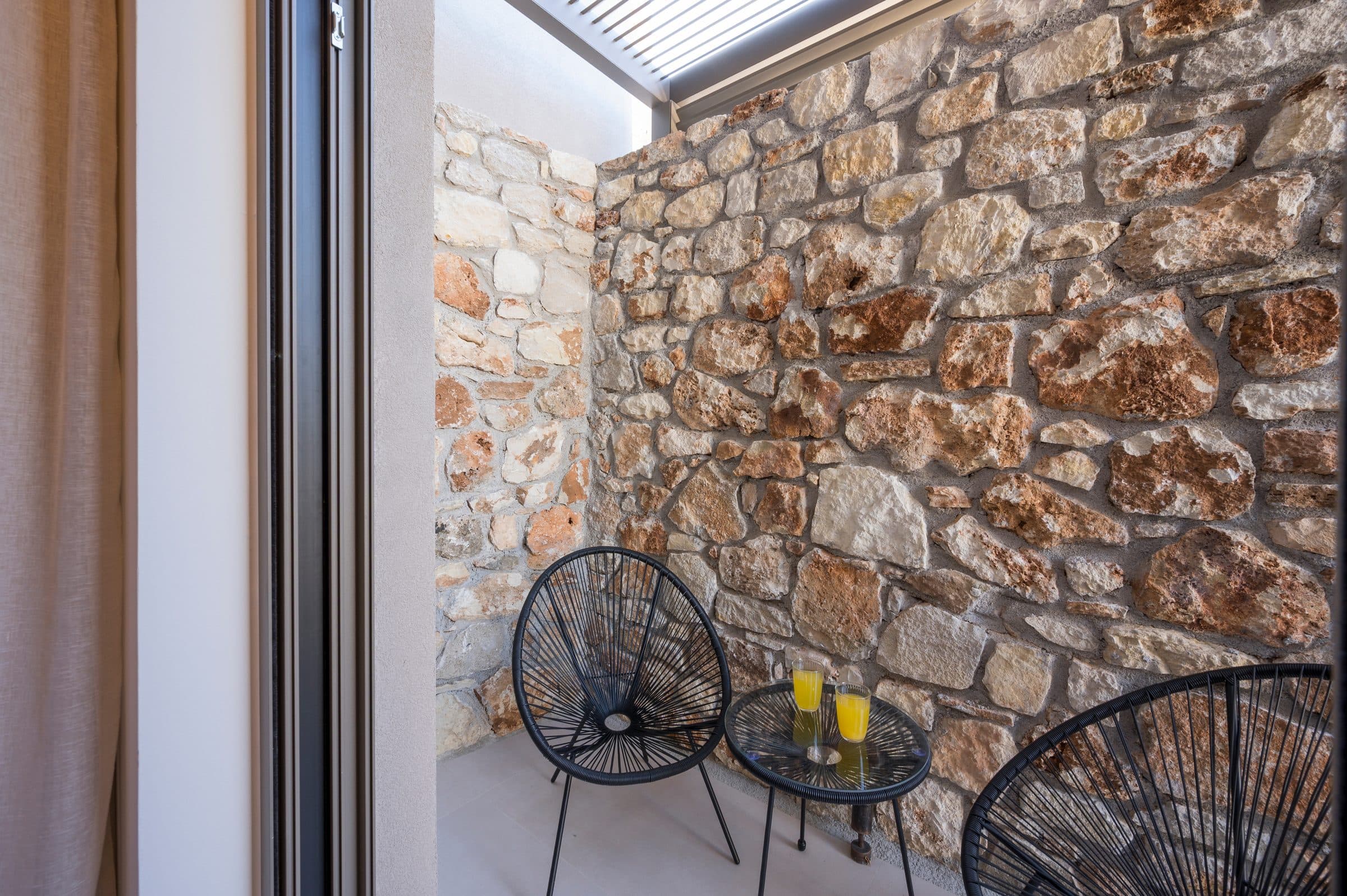 The sheltered stone courtyard seen from a bedroom doorway, with black wire chairs, a small table and two glasses of juice