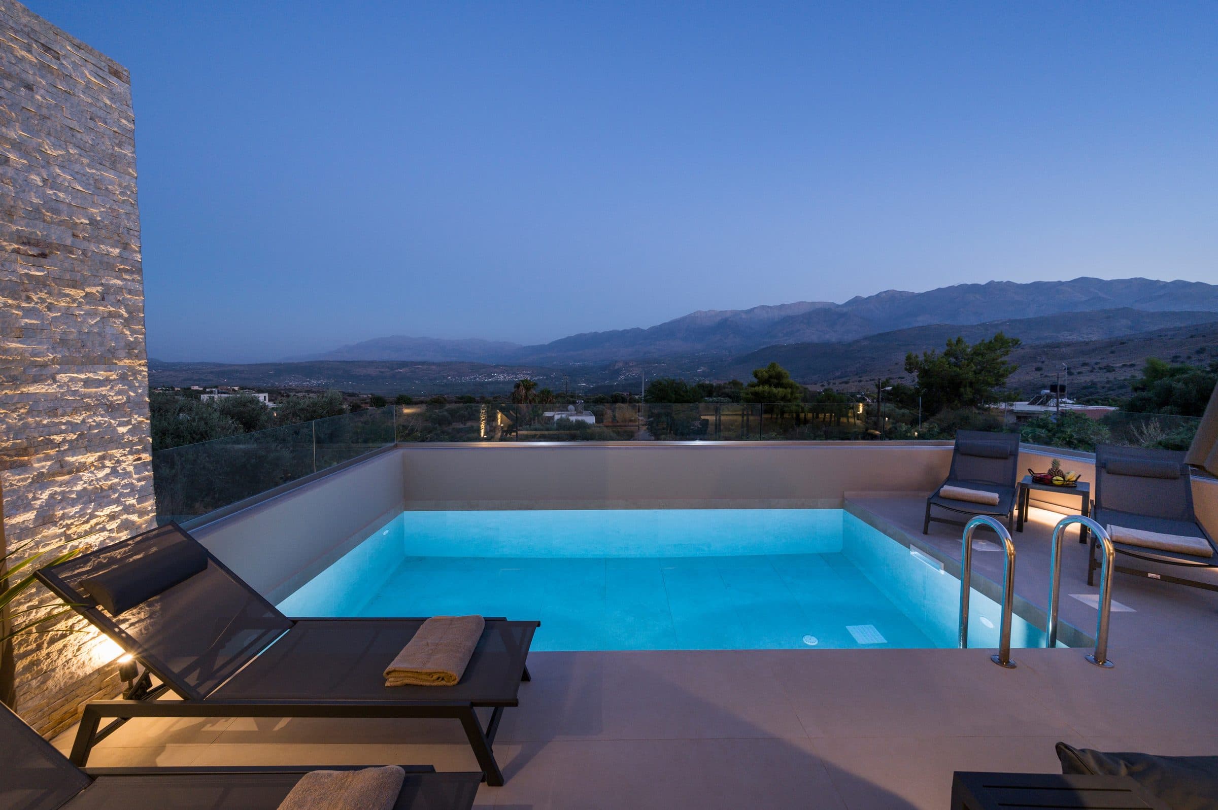 The pool glowing turquoise at blue hour beside the uplit stone wall, with the mountain ridge silhouetted behind