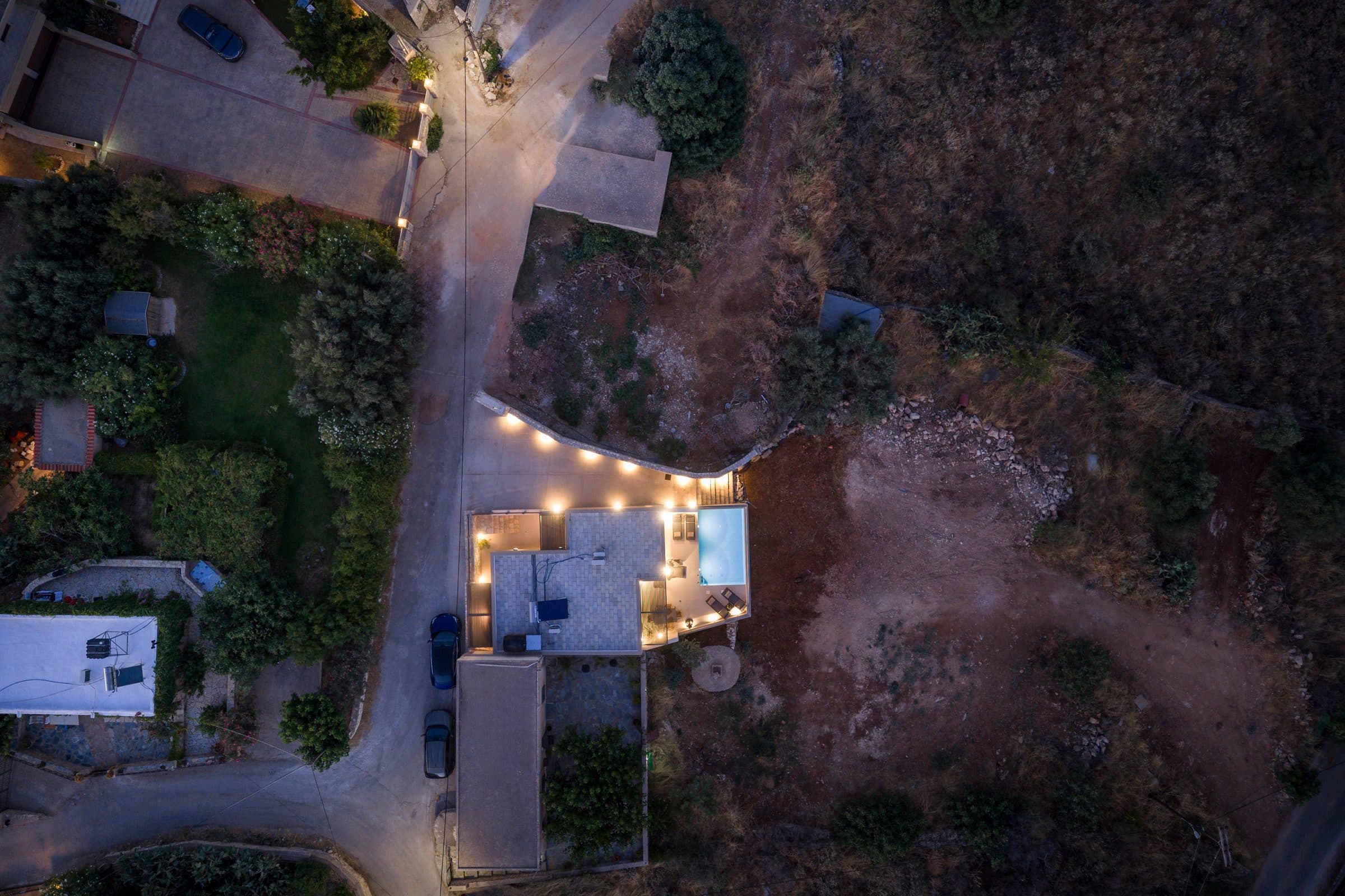 Drone view straight down onto the villa after dark, the terrace lights and glowing pool marking it out against the hillside