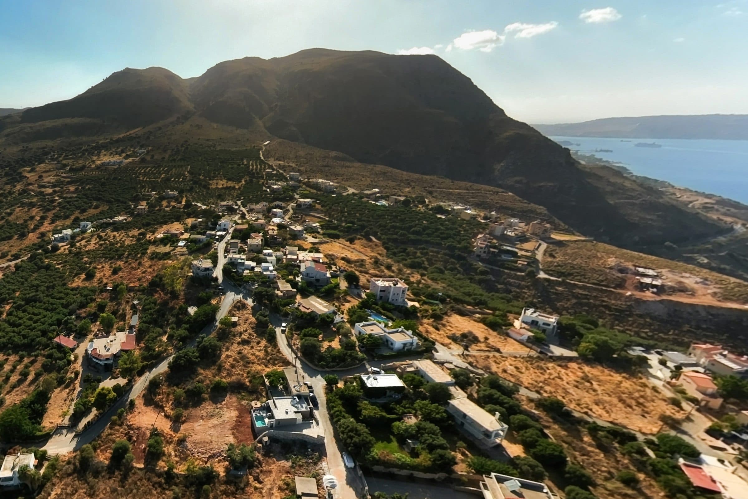 Aerial view of Megala Chorafia spread along the hillside beneath the Aptera ridge, with Souda Bay opening out to the right