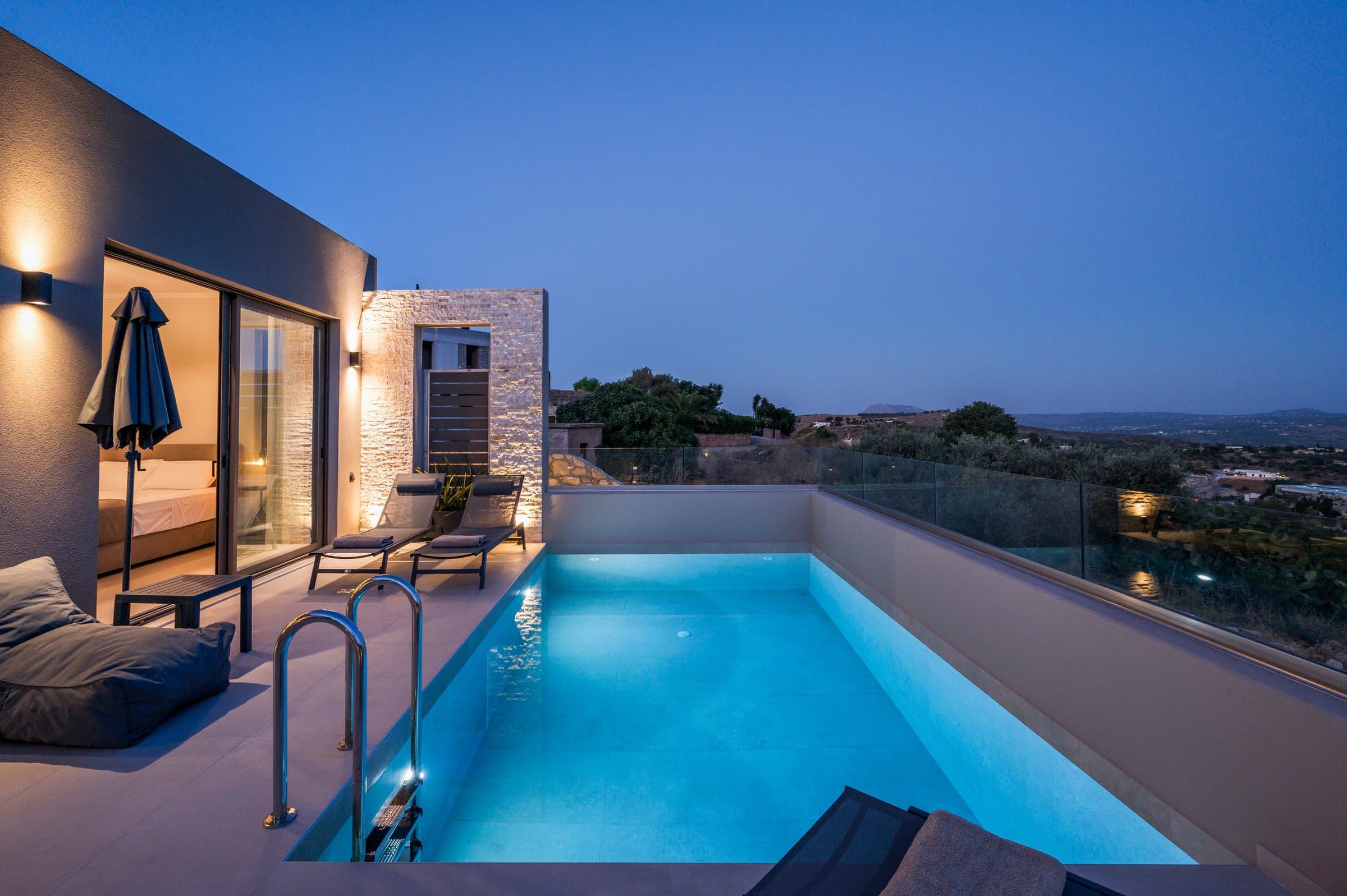 The private pool at blue hour, lit from within, beside the terrace and the warmly lit bedroom sliding doors